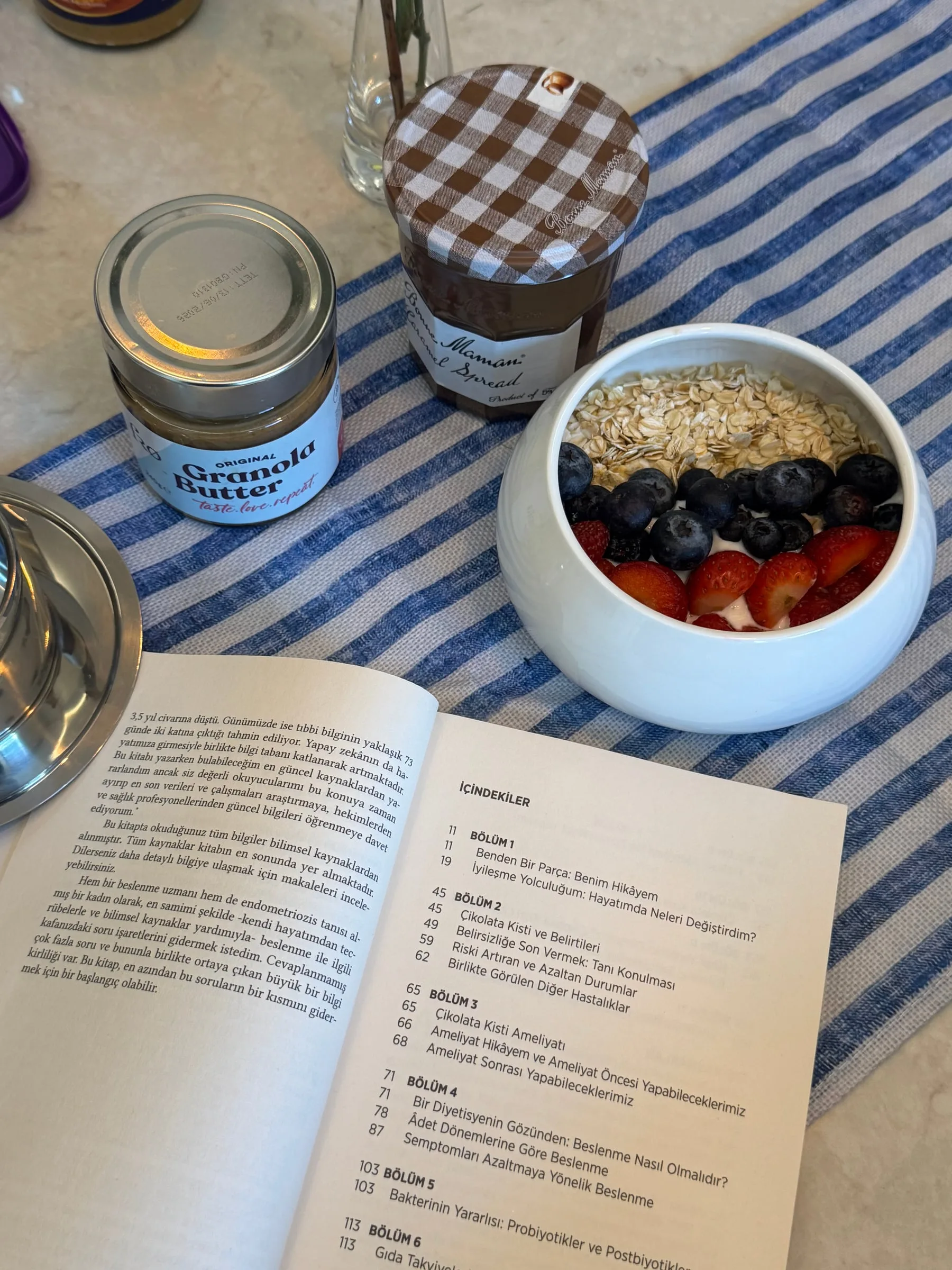 Part of Me lying open at the contents page, next to a bowl of yoghurt with strawberries, blueberries and oats, and two jars